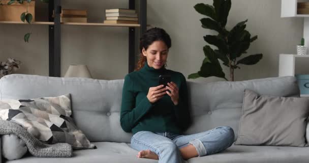 Sorrindo mulher relaxante no sofá usando telefone inteligente — Vídeo de Stock