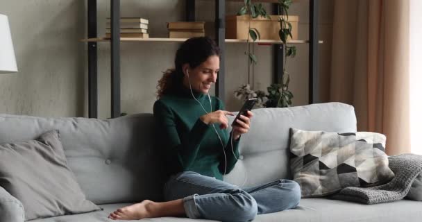 Mulher relaxante no sofá desgaste fones de ouvido com fio usar telefone inteligente — Vídeo de Stock