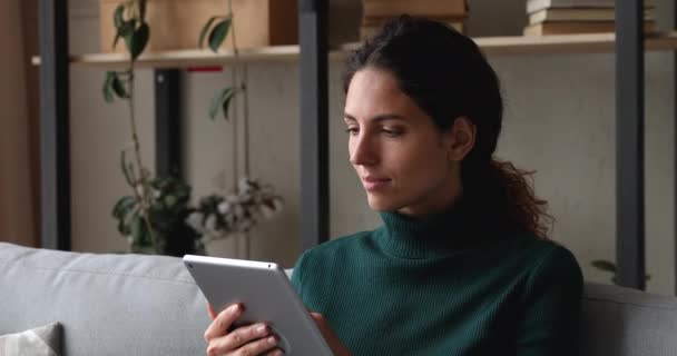 Mujer sonriente relajándose el fin de semana con el dispositivo de la tableta en el sofá — Vídeos de Stock