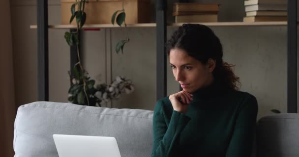 Pensivo feminino sentado no sofá pensando trabalhando no laptop — Vídeo de Stock