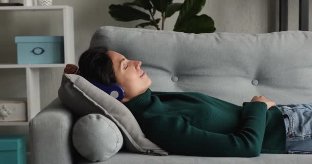 Donna sdraiata sul divano ascoltare musica attraverso cuffie wireless — Video Stock