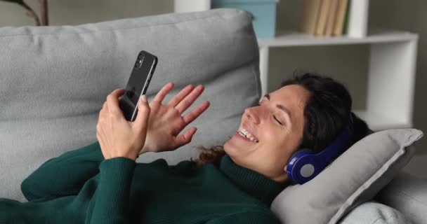 Mujer acostada en el sofá sosteniendo el teléfono móvil hablando por videocall — Vídeos de Stock