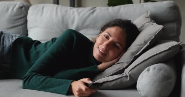 Ленивая женщина лежит на диване держа пульт дистанционного управления каналов — стоковое видео
