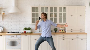 Gülümseyen genç adam mutfakta yemek pişirip dans ederken iyi eğlenceler.