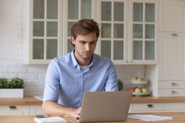 Genç beyaz adam evde dizüstü bilgisayarda çalışıyor.