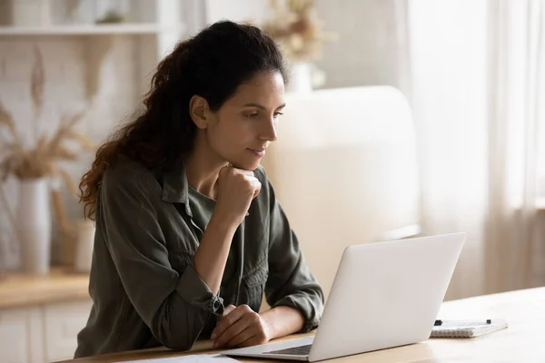 Молода жінка сидить за столом, працює на ноутбуці онлайн — стокове фото