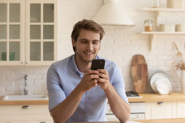 Uomo sorridente rilassarsi a casa utilizzando smartphone moderno — Foto Stock