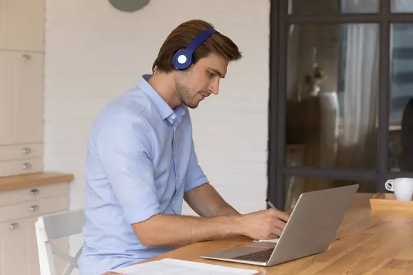 Millennial man in oortelefoons werken online op laptop — Stockfoto