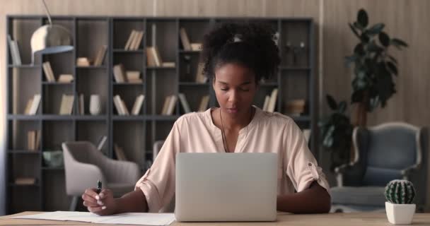 African woman using laptop working on financial paperwork seated indoor — Stock Video