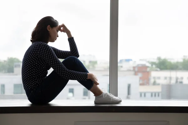 Depressed millennial korean mixed race woman sitting on windowsill. — Stock Photo, Image