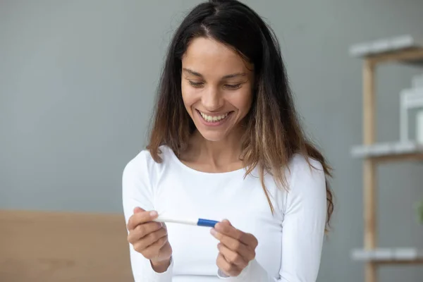 Крупным планом улыбающаяся женщина проводит тест на беременность, взволнованная результатом — стоковое фото