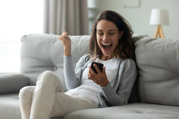 Радостная женщина пользуется телефоном, читает хорошие новости, празднует успех — стоковое фото