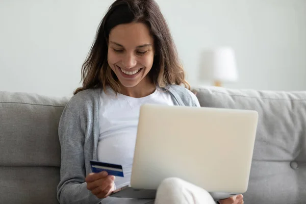 Blisko uśmiechnięta kobieta płaci online, za pomocą laptopa, trzymając kartę — Zdjęcie stockowe