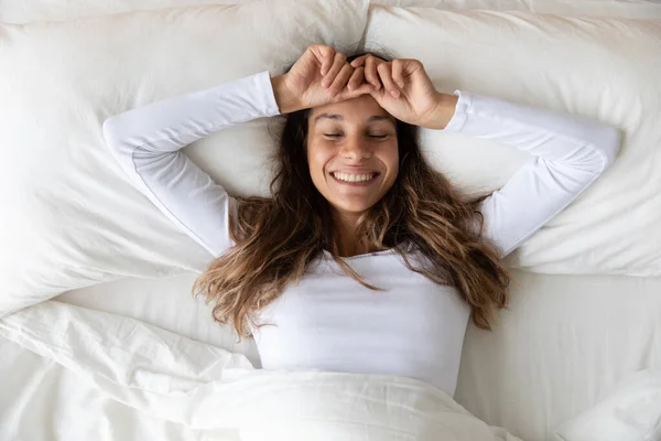Pandangan utama wanita muda tersenyum peregangan, berbaring di tempat tidur yang nyaman — Stok Foto