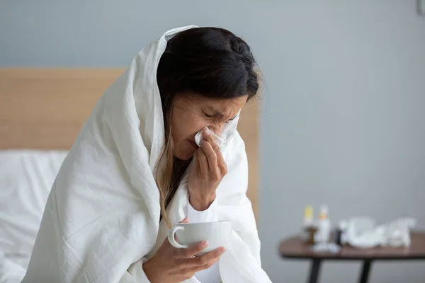 Close up mulher doente envolto em edredão quente soprando nariz — Fotografia de Stock