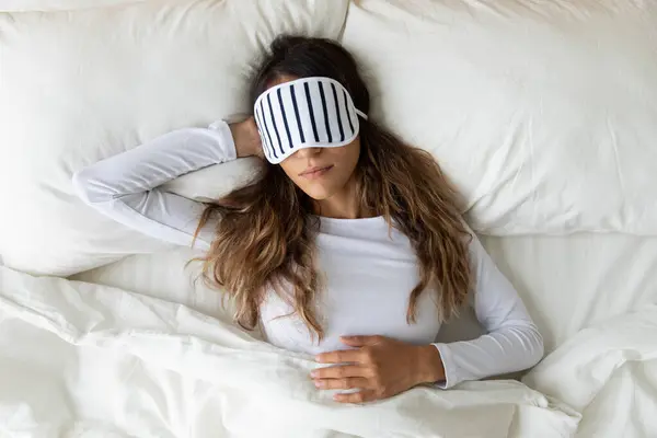 Top view calm woman wearing sleeping mask resting in bed