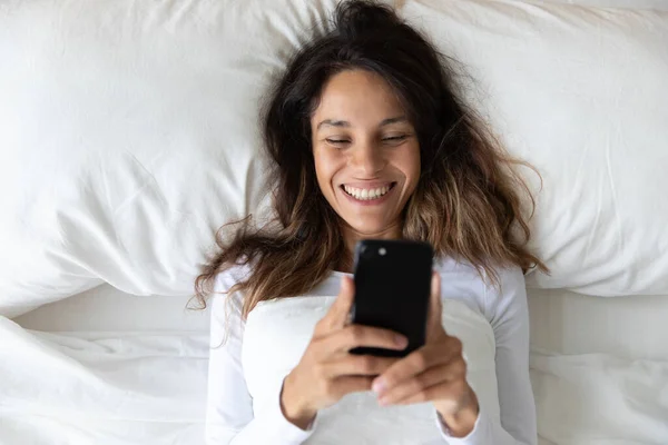 Vista dall'alto donna sorridente utilizzando il telefono, a riposo a letto — Foto Stock