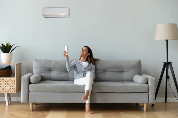 Glimlachende vrouw met airconditioner afstandsbediening, zittend op de bank — Stockfoto