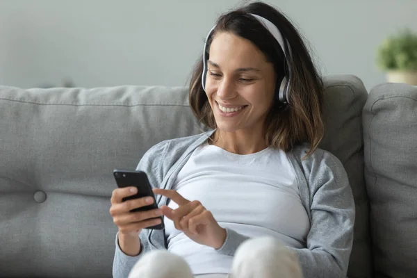 Close up smiling woman wearing headphones using phone at home — Stock Photo, Image