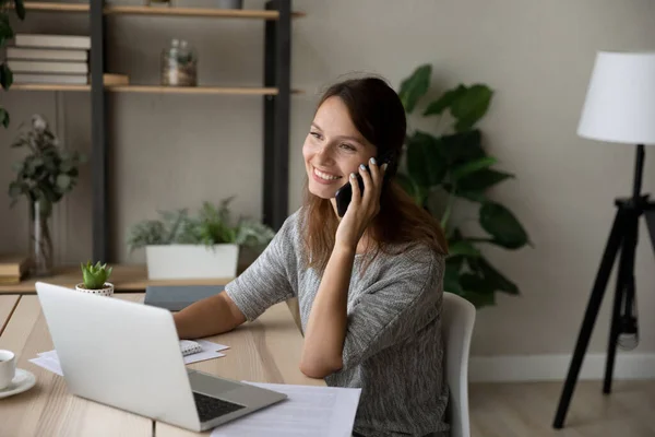 Smiling woman work on laptop talking on cellphone — Stock Photo, Image