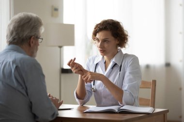 Ciddi yetenekli genç bayan doktor yaşlı hastaya tedaviyi açıklıyor..