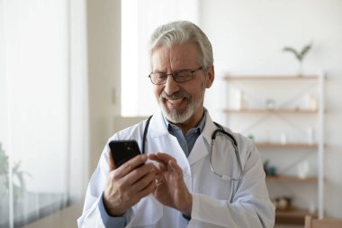 Klinikte cep telefonu kullanan mutlu yaşlı doktor..