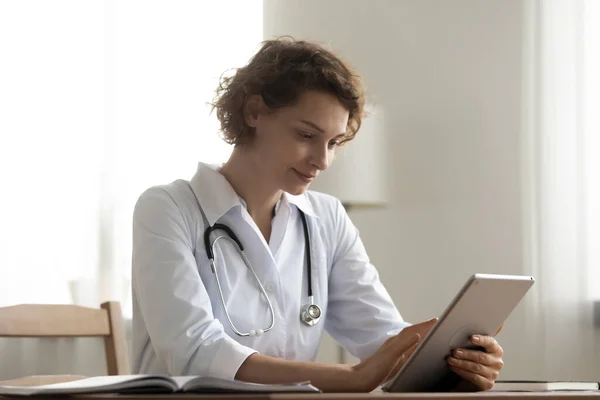 Pleasant happy female doctor general practitioner using digital computer tablet.