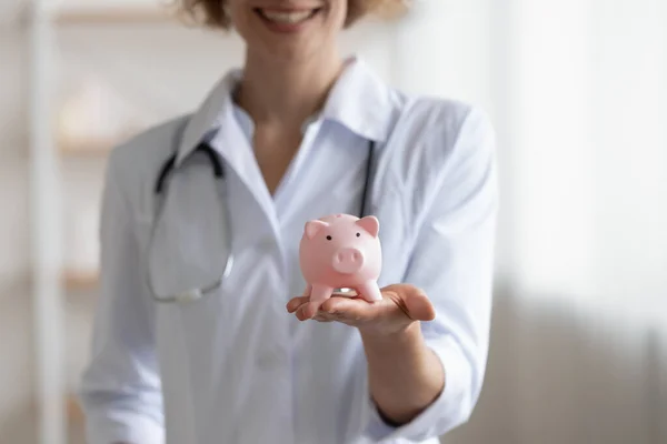 Close up smiling young doctor holding piggy bank in hands. — Stock Photo, Image