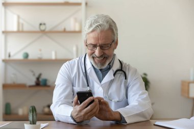 Gülümseyen olgun erkek doktor mobil uygulamalar kullanıyor..