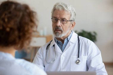 Genç hastayı dinleyen orta yaşlı, olgun, ağarmış bir doktor..