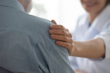 Genç mutlu bayan doktor yaşlı emeklilerin omzuna elini koyuyor..