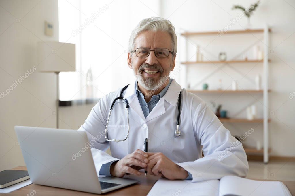 Portrait of smiling trusted middle aged old doctor at workplace.