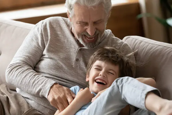 Heyecanlı büyükbaba oynuyor ve küçük çocuğu gıdıklıyor. — Stok fotoğraf