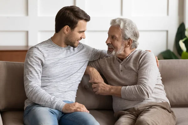 Elderly man talk with adult son on sofa at home — Stock Photo, Image