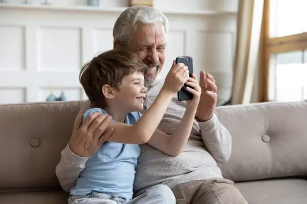 Smiling mature grandfather and little grandson use cellphone — Stock Photo, Image