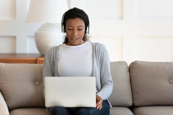 Sonriente millennial mujer de raza mixta en auriculares celebración de videollamada. — Foto de Stock