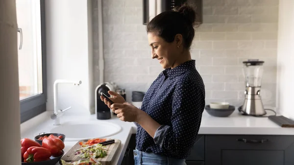 Smiling woman cook at home kitchen using smartphone — Stock Photo, Image