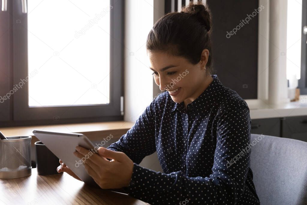Smiling Indian woman use modern tablet at home