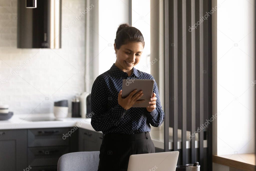 Smiling Indian woman use tablet texting online