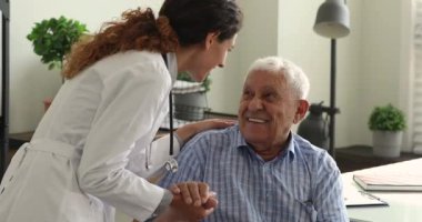Genç doktor sohbet sırasında yaşlı bir erkeğin elini tutuyor.