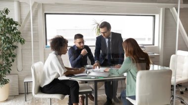 Çok ırklı meslektaşlar ofis yönetim kurulunda toplanmış evrak işlerini tartışıyorlar.