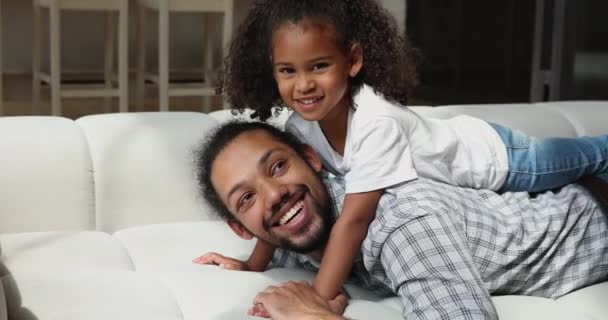 Africano filha deitada no papai de volta sorrindo olhando para a câmera — Vídeo de Stock