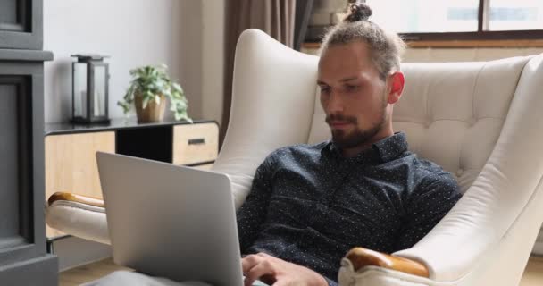 Mladý muž pracující na notebooku sedícím na pohodlném křesle — Stock video