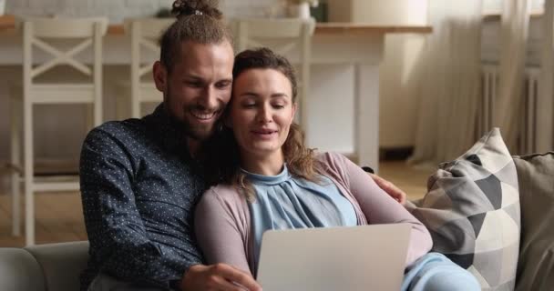 Mutlu genç çift evdeki kanepede dizüstü bilgisayarlarıyla dinleniyor. — Stok video