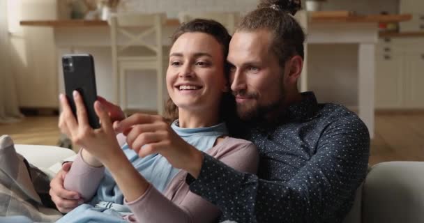 Pareja relajándose en el sofá divirtiéndose con el teléfono inteligente — Vídeos de Stock