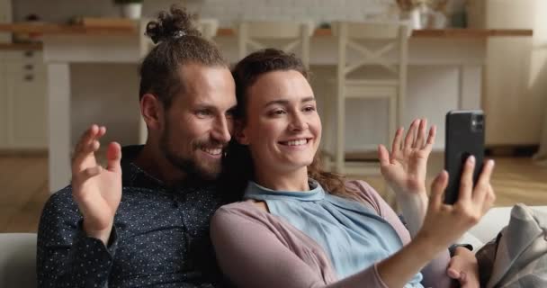 Pareja joven relajándose en el sofá hablando por videoconferencia utilizando el teléfono inteligente — Vídeos de Stock