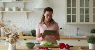 Elinde tablet olan genç bir kadın internette sağlıklı yemek tarifleri arıyor.