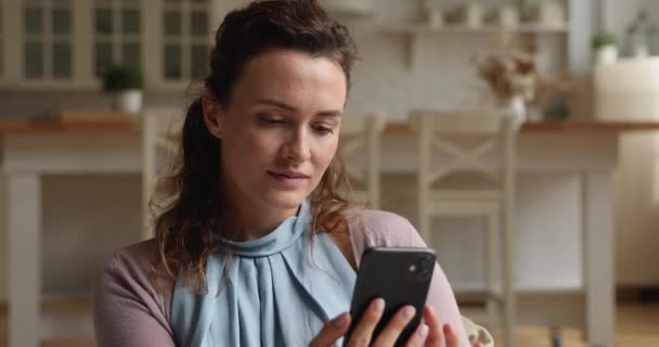 Snící mladá žena pomocí smartphone sedí na gauči uvnitř — Stock video