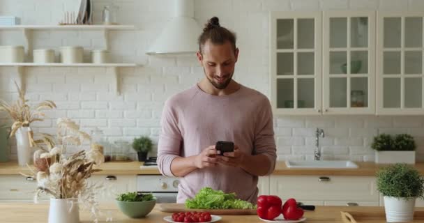 Hombre joven soltero sosteniendo teléfono inteligente buscar recetas de alimentos saludables en línea — Vídeo de stock