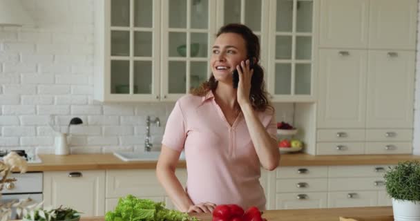 Mujer de pie en la cocina distraída de cocinar hablando en el teléfono inteligente — Vídeos de Stock